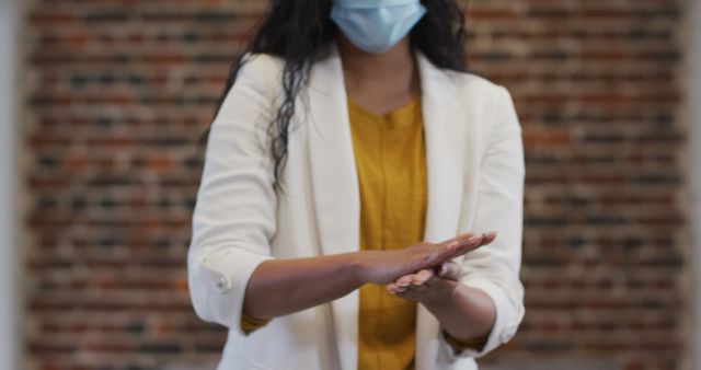 Woman in white blazer using hand sanitizer in a modern office environment. Perfect for illustrating pandemic work safety practices, hygiene protocols, workplace health standards, and COVID-19 prevention measures.