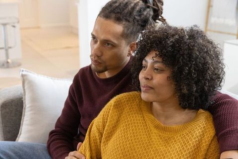 African american couple sitting closely on sofa wearing mustard and burgundy sweaters