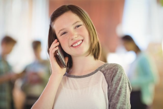 Smiling schoolgirl talking on mobile phone in corridor at school