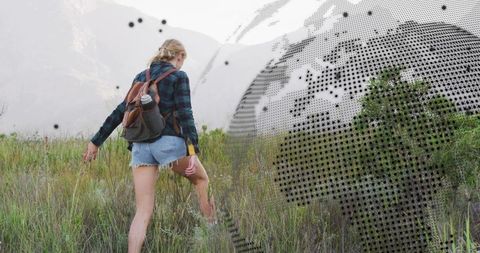 Solo hiker exploring mountain meadow with backpack, water bottle and digital globe overlay