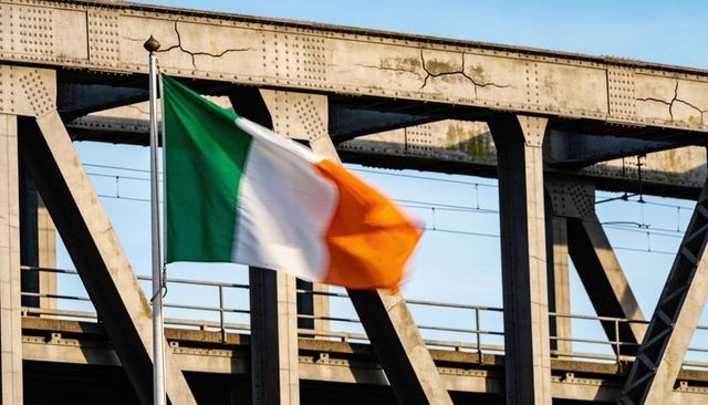 Irish tricolour fluttering on flagpole before urban riveted steel viaduct with motion blur