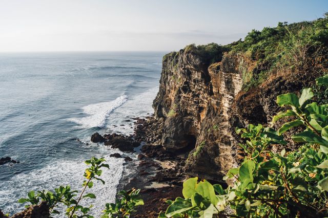 Spectacular coastal cliff during sunrise with crashing waves and rich greenery. This majestic scene can be used in travel brochures, nature websites, and outdoor adventure ads to inspire wanderlust and showcase the beauty of coastal landscapes.