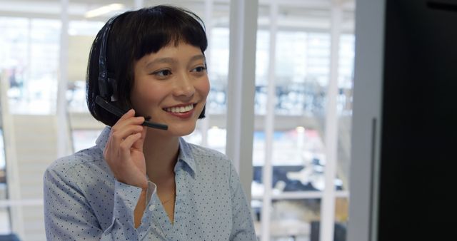 Woman in business attire wearing a headset while providing customer service in a bright, modern office environment. Ideal for conveying professionalism, customer support, communication, and teamwork. Suitable for use in blogs about business, customer service training materials, corporate websites, and promotional materials for communication services.