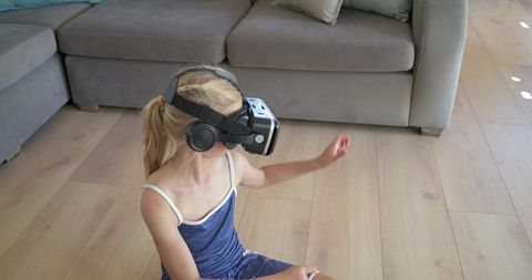 Young girl exploring virtual reality at home wearing headset headphones with controller