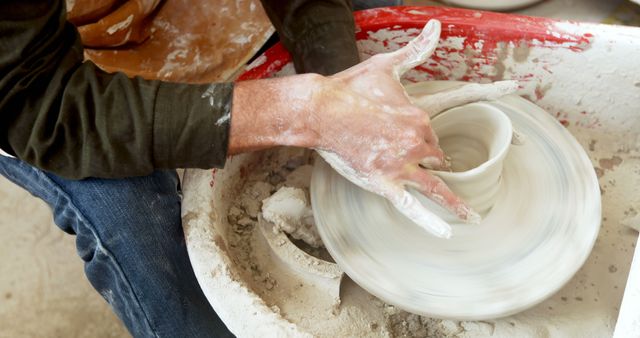 Close-up of hands shaping clay on a pottery wheel, capturing the process of creating ceramic art. This image is ideal for websites or publications about pottery techniques, artisan skills, or hands-on creative activities. It can also be used in content focusing on hobbies, craftsmanship, creative studios, or artistic expressions.