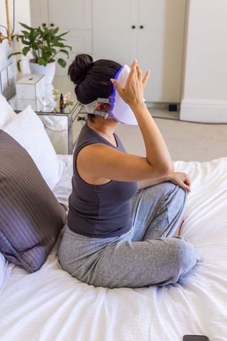 Woman using led facial mask on bed for at-home skincare and self-care ritual