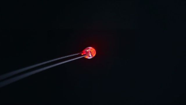 Macro red led glowing with concentrated halo on dark backdrop, minimal electronics close-up