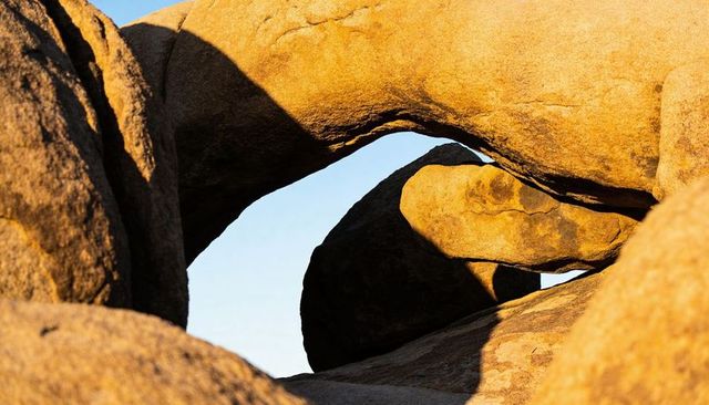 Sunlit granite arch framing round boulder and blue desert sky with warm textures