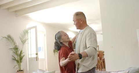 Senior asian couple dancing together in bright open living room with natural light