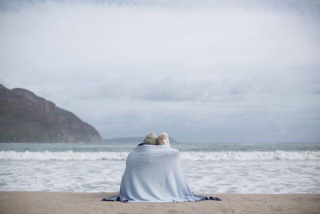 Rear view of mature couple wrapped in blanket on the beach