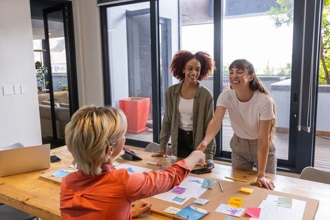 Diverse female coworkers shaking hands over office collaboration