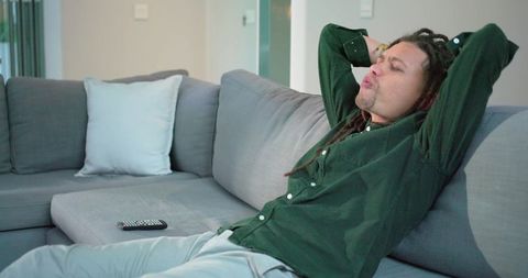 Relaxing man reclining on modern gray sectional sofa with remote and minimalist living room