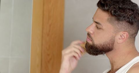 Man Grooming Beard with Wooden Brush in Minimalist Bathroom
