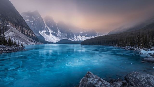 Turquoise Glacial Lake Reflecting Pink Sky in Misty Alpine Valley at Sunrise