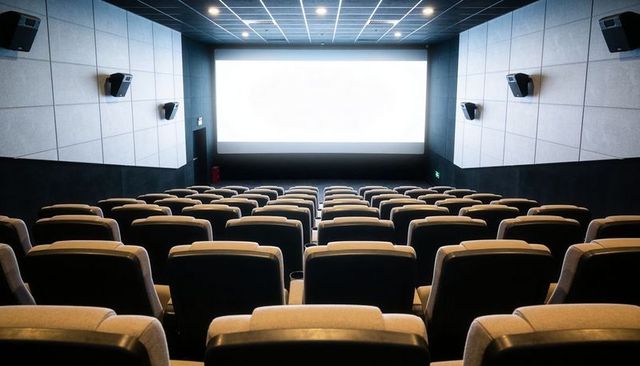 Modern empty cinema auditorium with upholstered seating rows facing bright blank projection screen