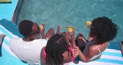 African american friends relaxing poolside with citrus cocktails and striped towels