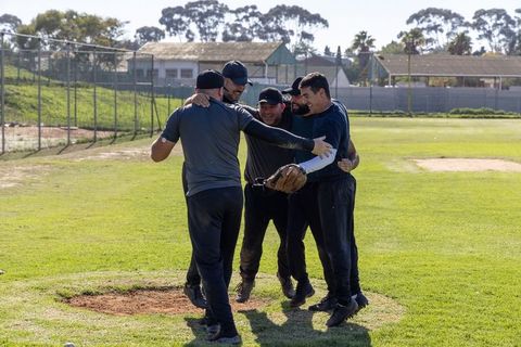 Baseball teammates celebrating run, huddling on pitcher's mound, showing teamwork and joy