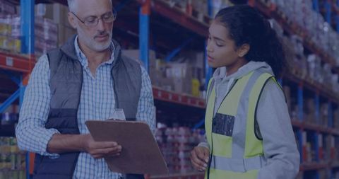 Warehouse supervisor reviewing inventory with associate holding clipboard in aisle