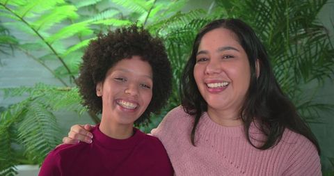 Diverse women smiling together at home wearing cozy knit sweaters with lush indoor plants