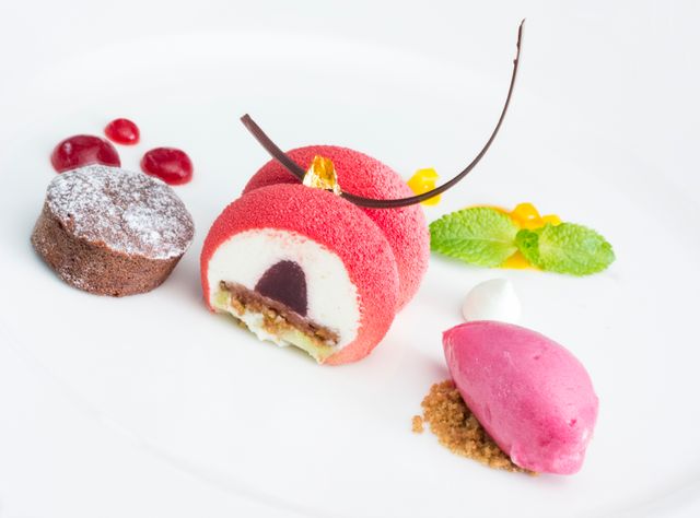 This high-end gourmet plate features an elegantly presented raspberry dessert, complete with mousse, sorbet, chocolate garnish, and various delicate sweets and garnishes. Ideal for showcasing culinary arts, fine dining menus, food blogs, or advertisements for luxury restaurants. Perfect for illustrating elegance and sophistication in food presentation.