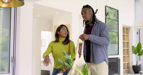 Diverse couple carrying groceries and talking in bright modern home entryway
