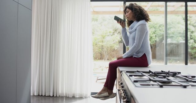 Woman Sitting on Kitchen Counter Using Smartphone at Home - Download Free Stock Images Pikwizard.com