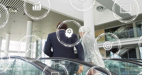 Business duo ascending glass escalator in modern atrium with technology overlay icons