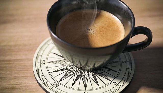 Steaming black ceramic cup on compass rose coaster with espresso crema, warm morning
