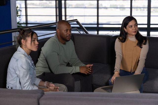 Diverse team collaborating on laptop in modern office lounge with waterfront view