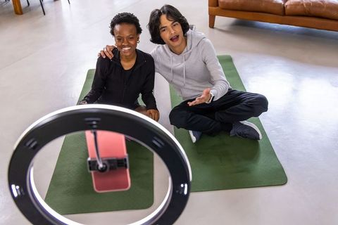 Diverse friends recording home workout with ring light and smartphone on yoga mats