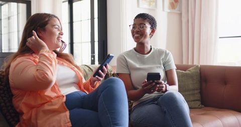Friends Sharing Laughter and Smartphones on Cozy Sunlit Living Room Sofa