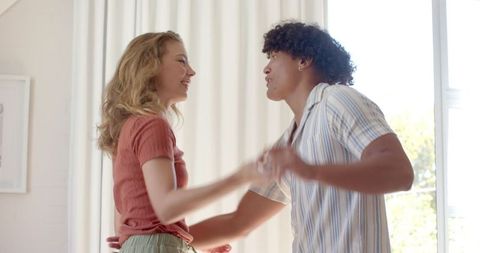 Couple dancing playfully in bright living room with curtains