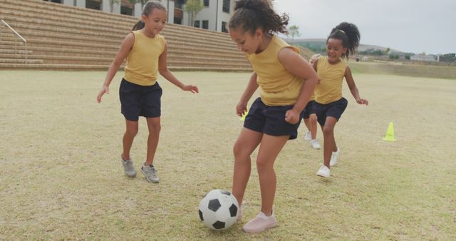 Image of happy diverse girls playing soccer in front of school. primary school education, sport and exercising concept.