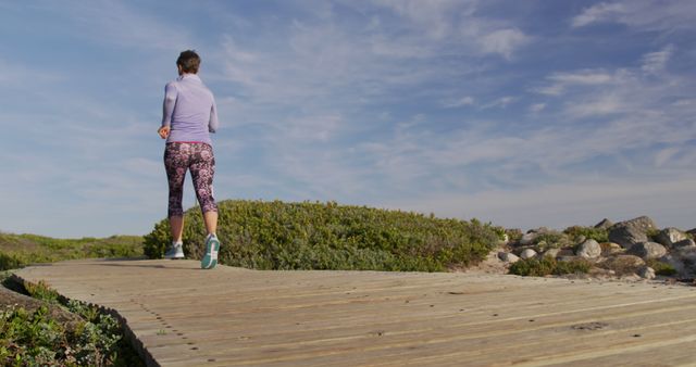 Woman Jogging on Wooden Path Near Beach Under Blue Sky - Download Free Stock Images Pikwizard.com