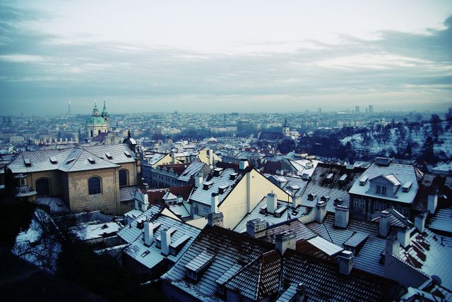 Snow-covered European city rooftops under a cold winter morning sky. Ideal for use in travel brochures, winter-themed advertising campaigns, holiday cards, and blogs focusing on winter travel destinations or European cityscapes. Evokes a cozy yet chilly atmosphere perfect for any winter-related content.