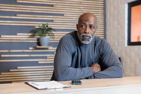 Leaning mature man at contemporary reception desk holding clipboard and smartphone