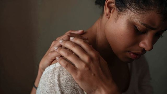 Reflective woman clasping shoulder in moody low light closeup for mental health self-care