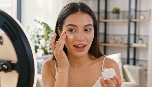 Beauty creator applying moisturizer to cheek with led ring light and clear jar