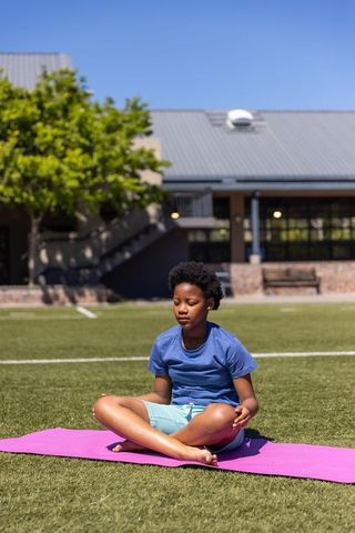 African american girl meditating cross-legged on pink yoga mat on school turf
