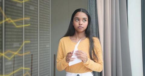 Standing woman holding torn paper by window in minimalist apartment, contemplative mood