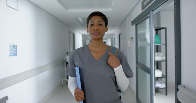 Ideal for use in healthcare-related websites, advertisements for medical services, brochures for hospital recruitment, and educational materials for nursing programs. It depicts a confident female nurse or healthcare worker walking in a hospital corridor, suggesting professionalism and dedication in the medical field.