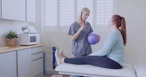 Physical therapist guiding patient with exercise ball for rehabilitation