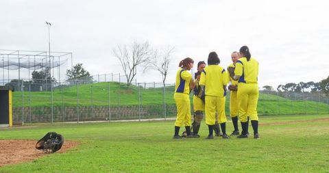 Female softball team in yellow uniforms huddling on field