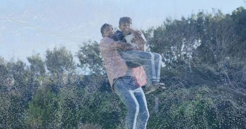 Indian father lifting son holding white dog on sunlit grassy slope, outdoor family bonding