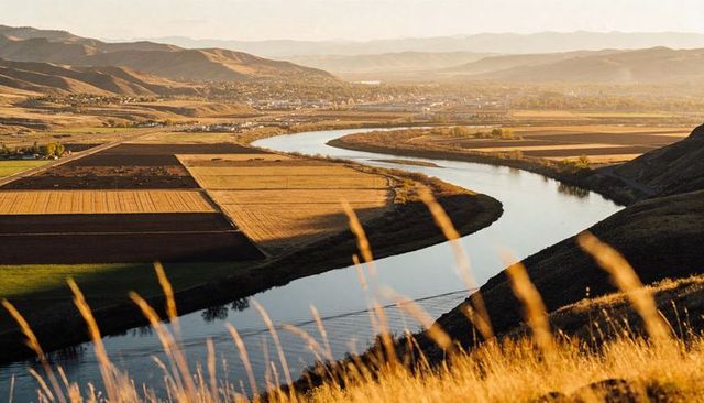Golden river meandering through cultivated fields and rolling hills at sunset