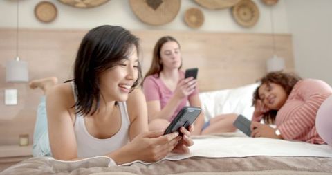 Diverse Young Women Lounging with Smartphones in Cozy Bedroom
