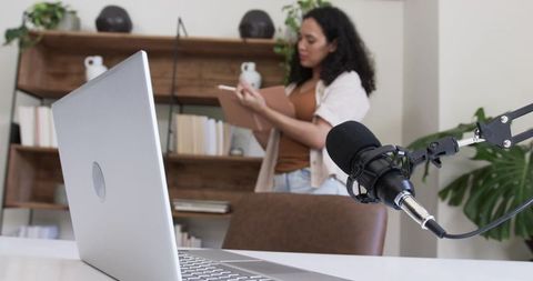 African american woman preparing podcast in home office with laptop and studio microphone