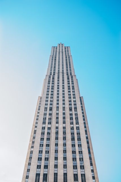 This photo of a towering skyscraper captures its impressive height against a clear blue sky. Perfect for use in urban studies, real estate presentations, and modern architecture features.