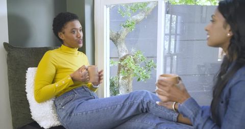 African American Friends Relaxing with Coffee by Window Seat