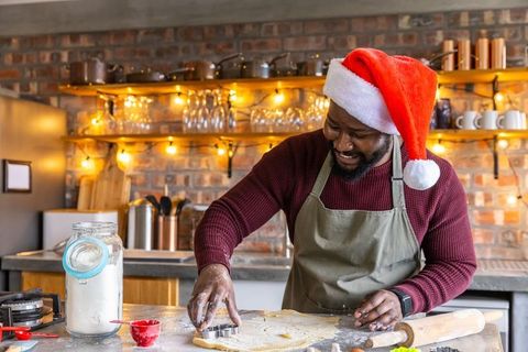 African American man wearing Santa hat baking Christmas cookies in rustic cozy kitchen